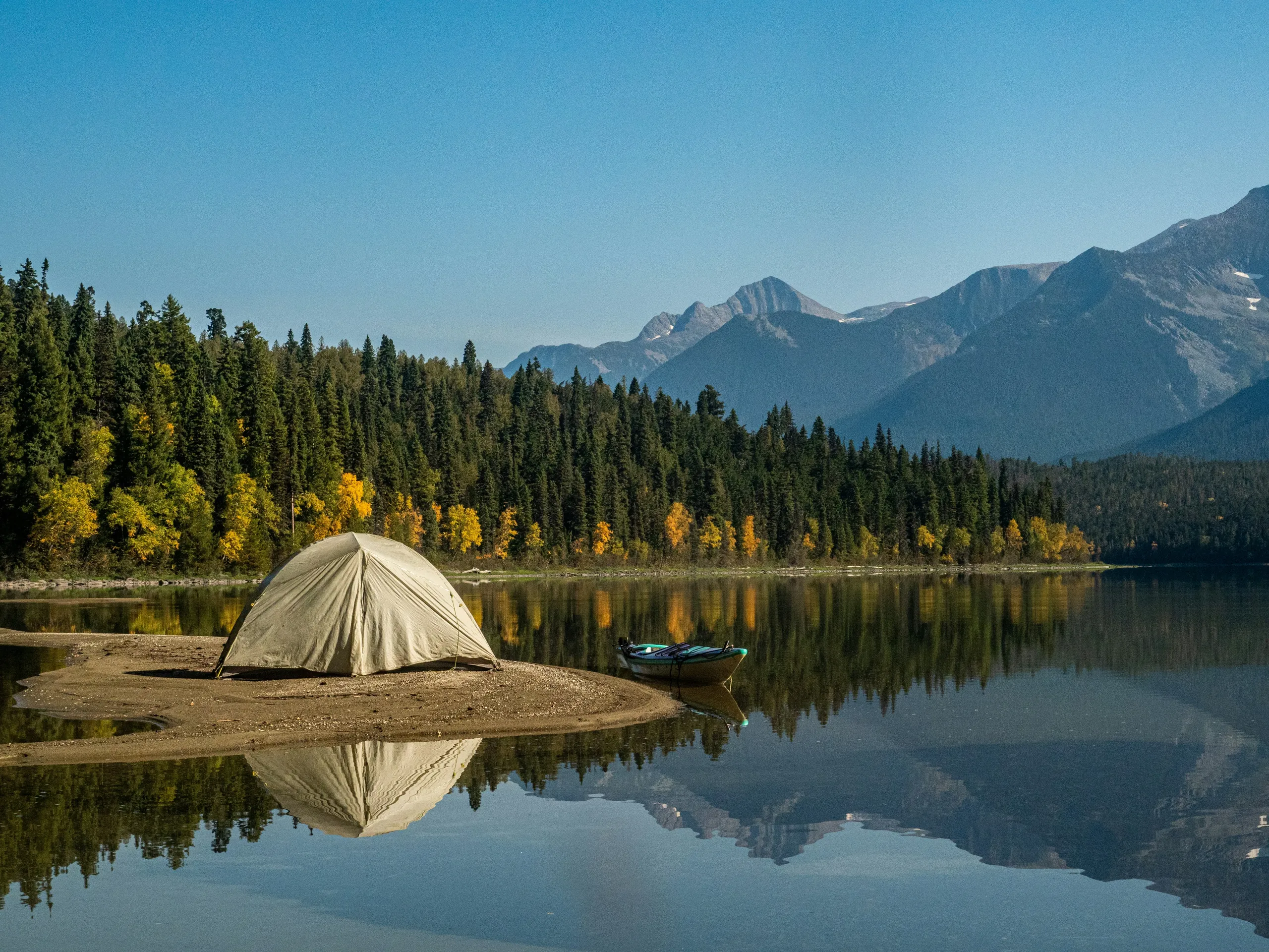 A tent pitched beside a mountain lake, with forested slopes behind it